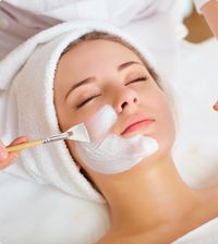 Entspannende Gesichtsbehandlung: Eine Kosmetikerin trägt mit einem Pinsel eine pflegende Creme-Maske auf die Haut einer Kundin auf.